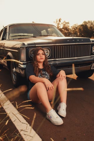 Woman sitting in front of a classic car in street fashion.