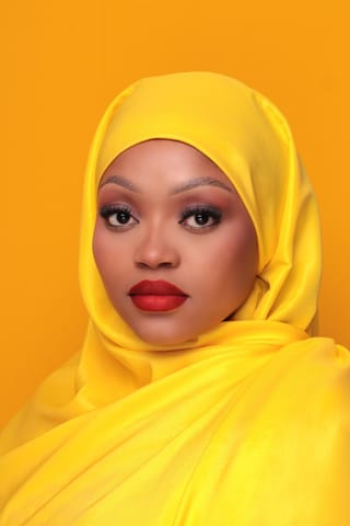 Woman wearing a bright yellow headscarf in a studio portrait.
