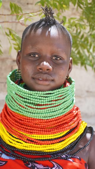 Child wearing colorful layered beaded necklaces outdoors.