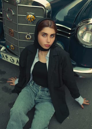 Woman in a black blazer posing beside a vintage car.
