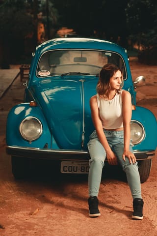Woman sitting in front of a blue Volkswagen Beetle.