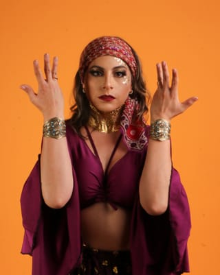Woman in colorful boho fashion and jewelry against an orange background.