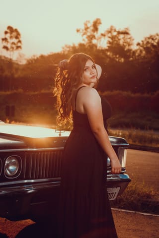 Woman in an evening dress beside a vintage car at sunset.