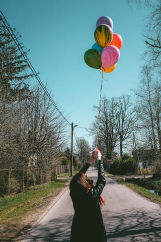 Woman holding colorful balloons on a country road.