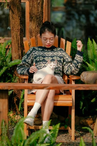Woman reading a book with a cat outdoors.