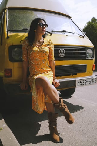 Woman in an orange dress beside a vintage van on a road trip.