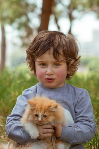 Young boy holding an orange kitten outdoors.
