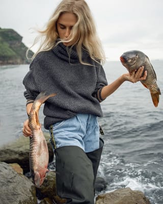Woman holding a fish on a rocky coast.
