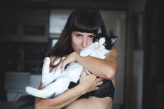 Woman hugging a black-and-white cat at home.