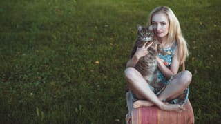 Woman holding a cat while sitting on grass.