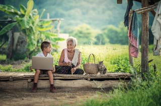 Grandmother and child using a laptop outdoors.