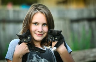 Young woman holding a black cat outdoors.