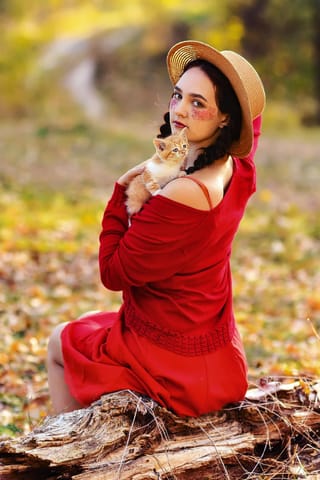 Woman in a red dress holding a cat in autumn.