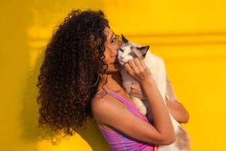 Woman kissing a cat in a colorful studio portrait.