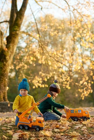 Children playing toy trucks autumn park.