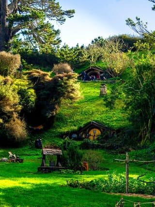Green hobbit houses lush countryside landscape.