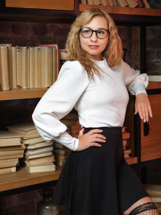 Red-haired woman glasses white blouse black skirt library.