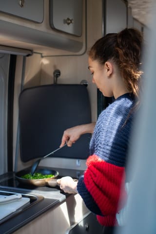 Woman cooking campervan kitchen road trip.