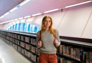Woman library aisle bookshelves student portrait.