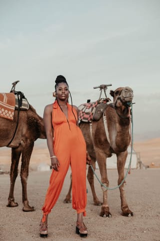 Woman orange jumpsuit camels desert travel.